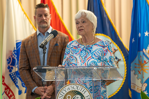 U.S. Rep. Greg Steube listens as USF Sarasota-Manatee Regional Chancellor Karen Holbrook, standing behind a podium, discusses a new cybersecurity training program being offered by the university. 